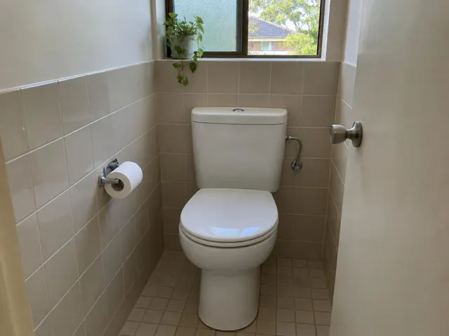 Clean white toilet in a tiled bathroom with a window and towel rail in St Ives